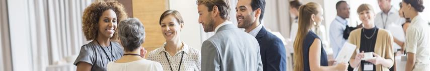 Image shows group of well dressed business men and women stood talking after conference meeting